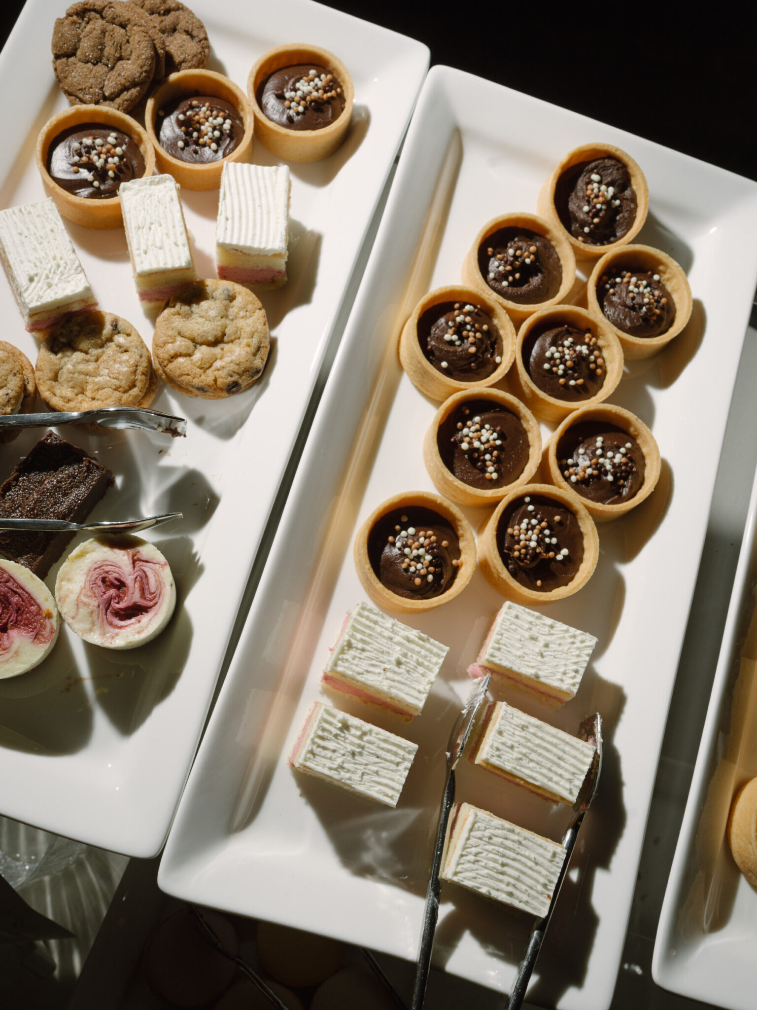 Assorted mini desserts arranged on white trays, including layered cake slices, chocolate tarts with sprinkles, cookies, and other pastries—perfect for elegant wedding catering in Seattle, all beautifully viewed from above.