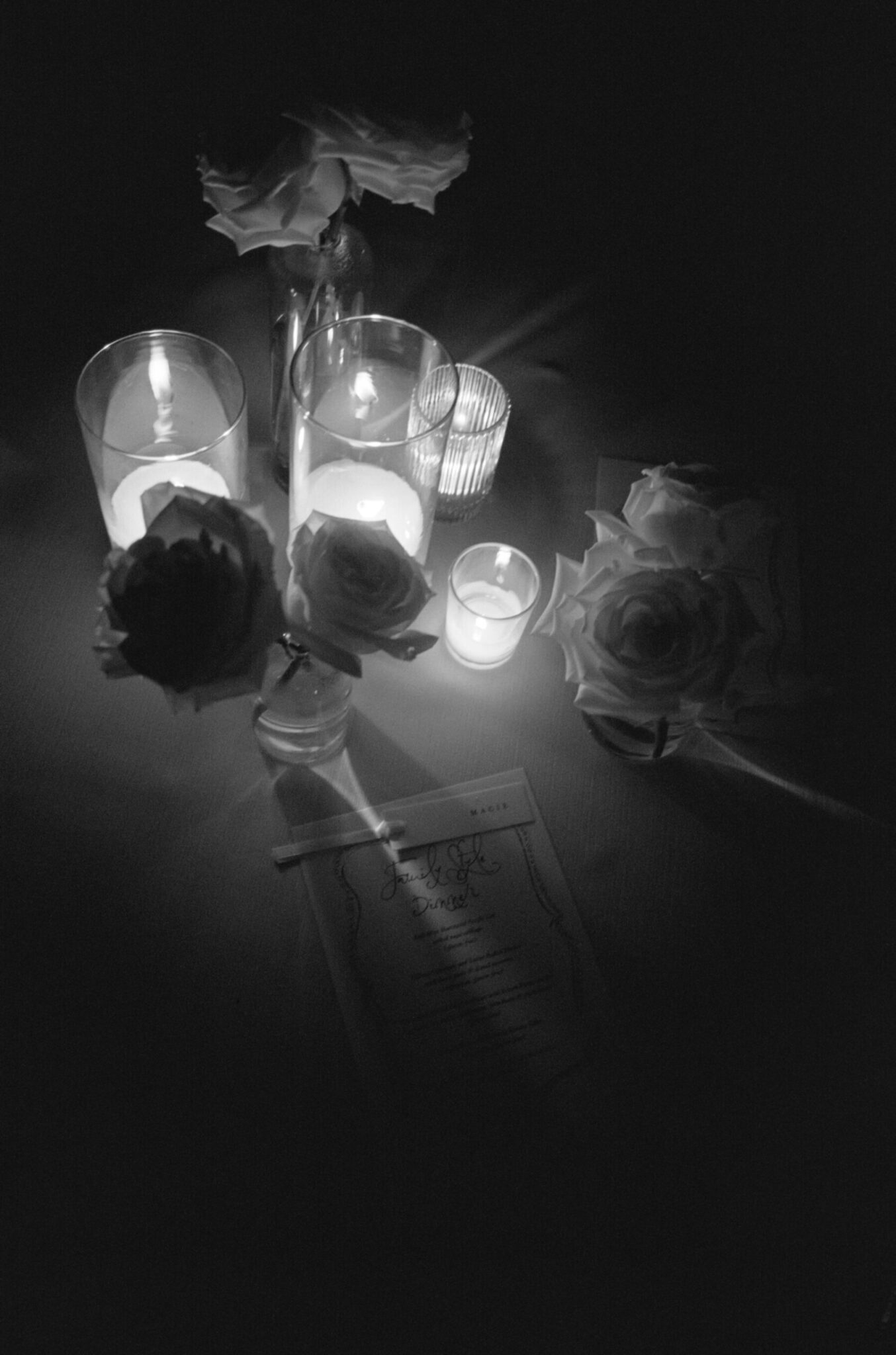 Black and white image of a table with lit candles, flowers in small vases, and a printed menu, capturing the elegant ambiance of wedding catering Seattle.