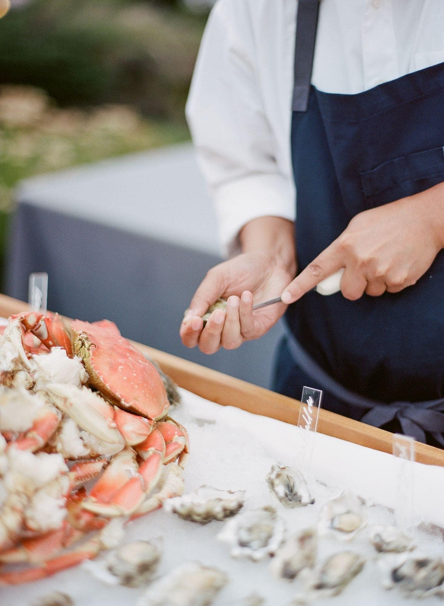 A person in a navy apron shucks oysters at a seafood station with crabs and oysters displayed on ice, showcasing the freshness and elegance of wedding catering Seattle style.