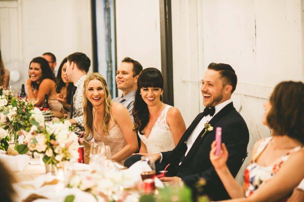 A group of people in formal attire sit at a decorated table, smiling and laughing during a wedding reception featuring elegant wedding catering Seattle style.