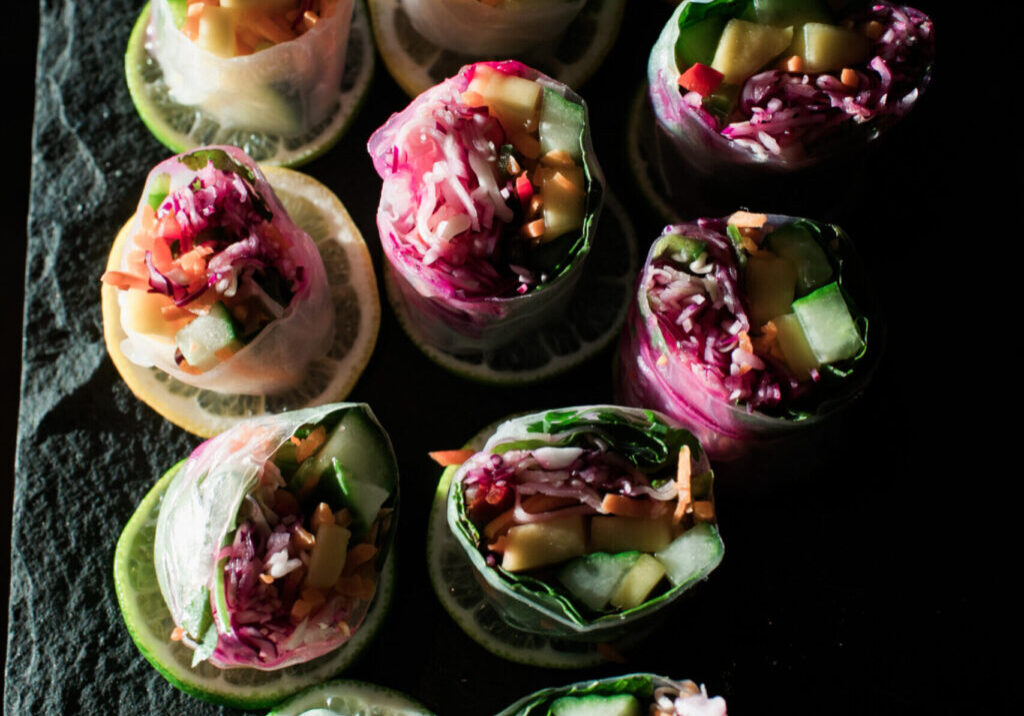 Vegetable spring rolls filled with julienned vegetables and leafy greens, arranged on lemon and lime slices atop a dark surface—perfect for fresh, vibrant corporate catering in Seattle.
