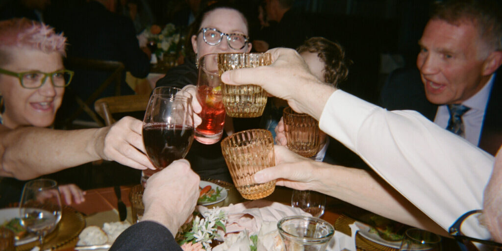 A group of people seated around a table raise their glasses for a toast at a formal event, with plates of food and flowers—beautifully arranged by expert wedding and event catering—visible on the table.