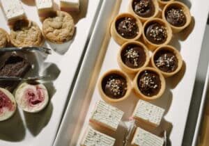An assortment of cookies, layered wafer snacks, and chocolate tarts with sprinkles displayed on white trays.