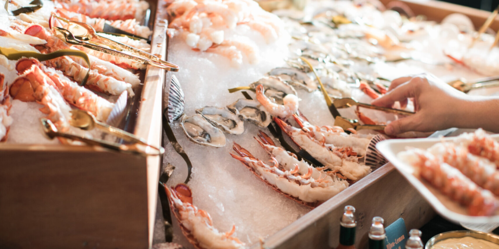 A seafood buffet display with lobster, shrimp, oysters, and crab on ice showcases the premium offerings of Catering Services in Seattle, complete with serving tongs and a guest selecting fresh seafood.